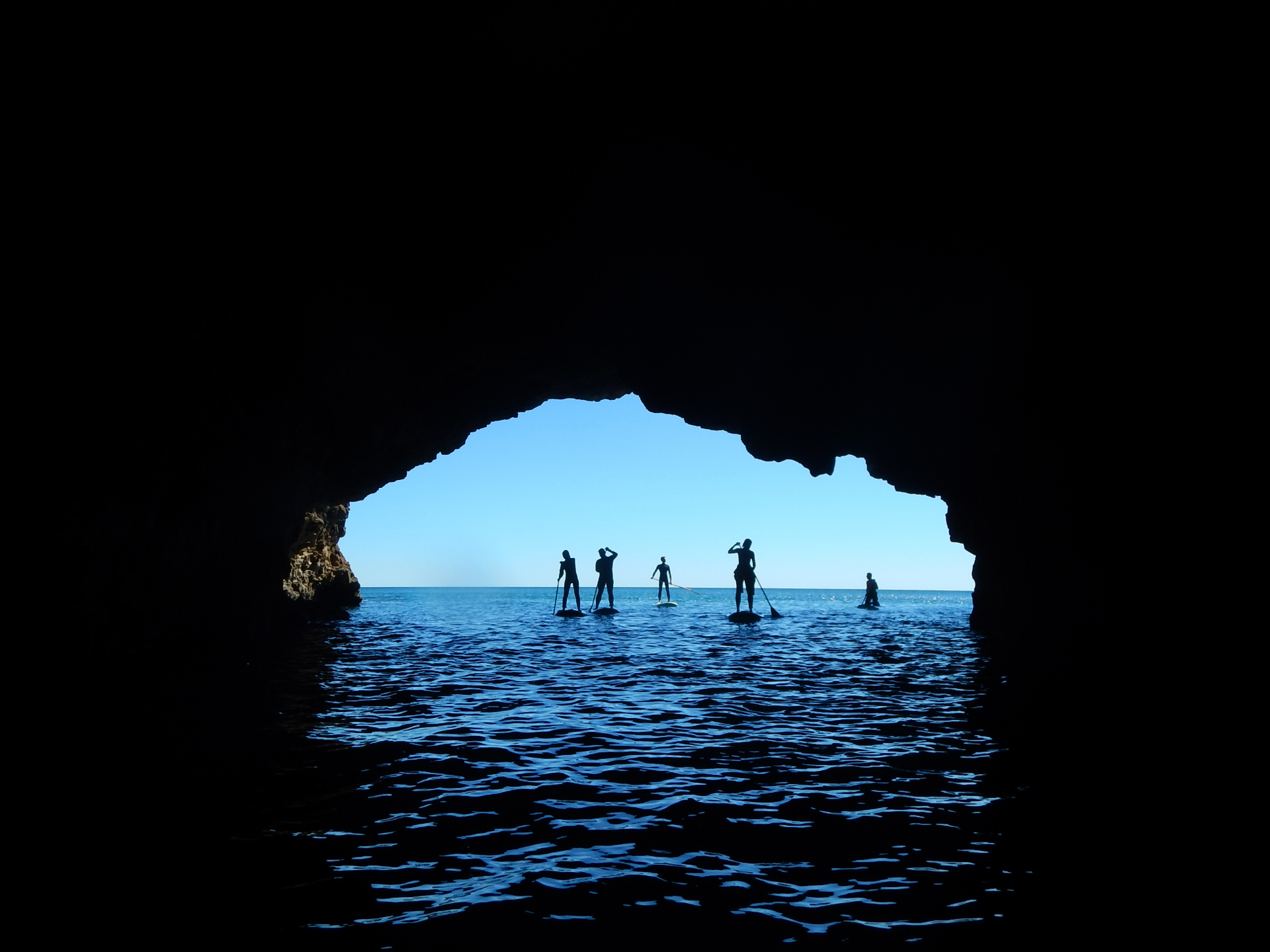 Stand Up Paddlers em silhueta dentro de uma gruta marinha dourada do Algarve